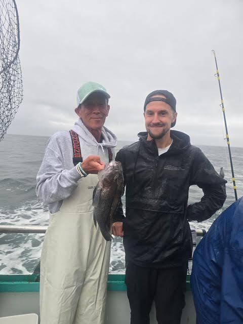 Two people on a boat holding a fish, cloudy sky in background.