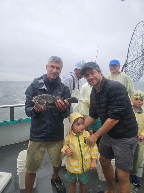 Group photo on boat with fish caught, gray sky background.