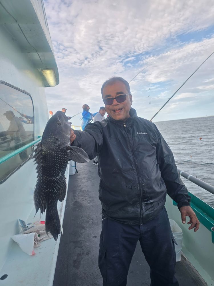 Man on boat holding a fish, smiling, with ocean in the background.