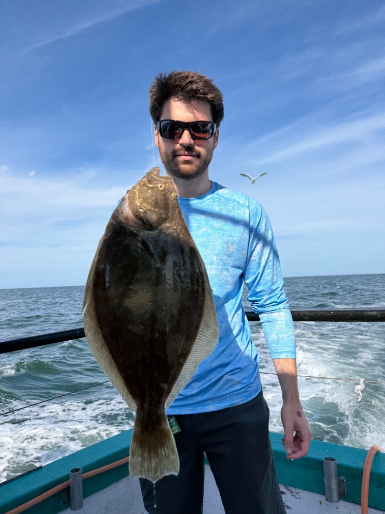 Person holding a flatfish on a boat with ocean in the background.