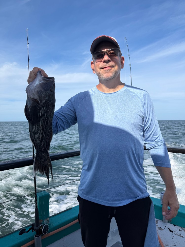 Man in sunglasses holding a fish on a boat with ocean in the background.