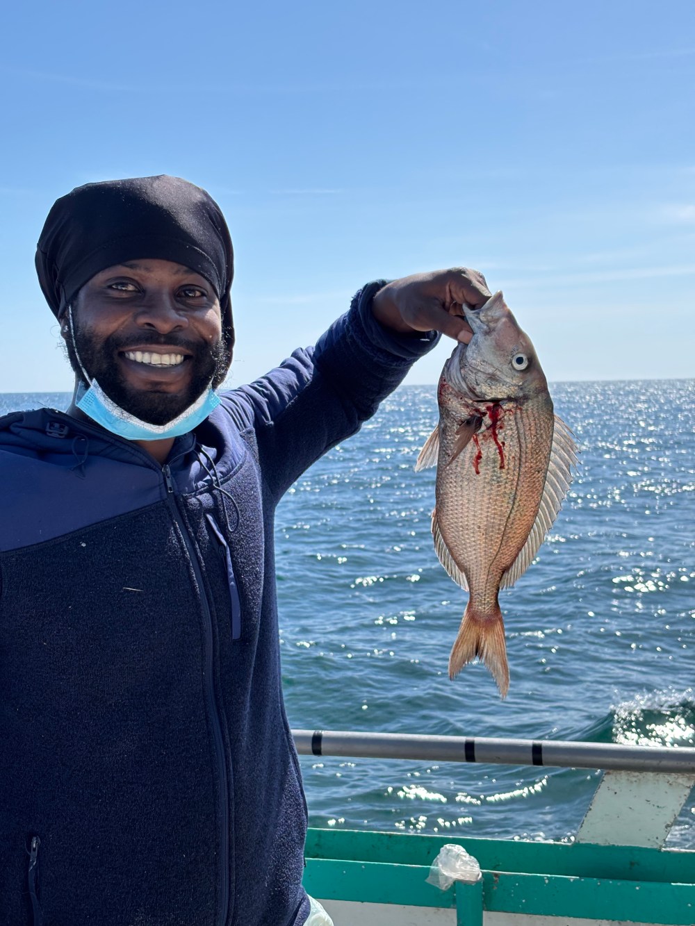 Person holding a fish on a boat with the ocean in the background.