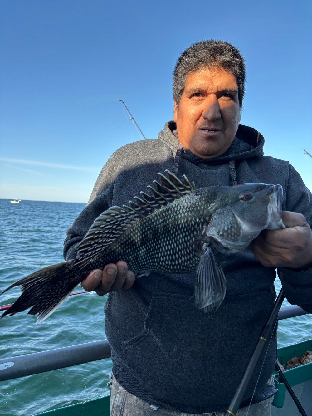 Man holding a fish on a boat, ocean in the background.