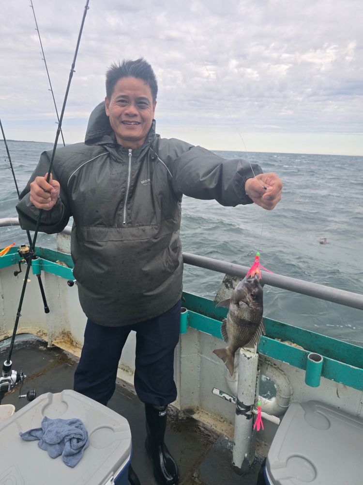 Person holding fish on a boat with fishing gear and cloudy sky.