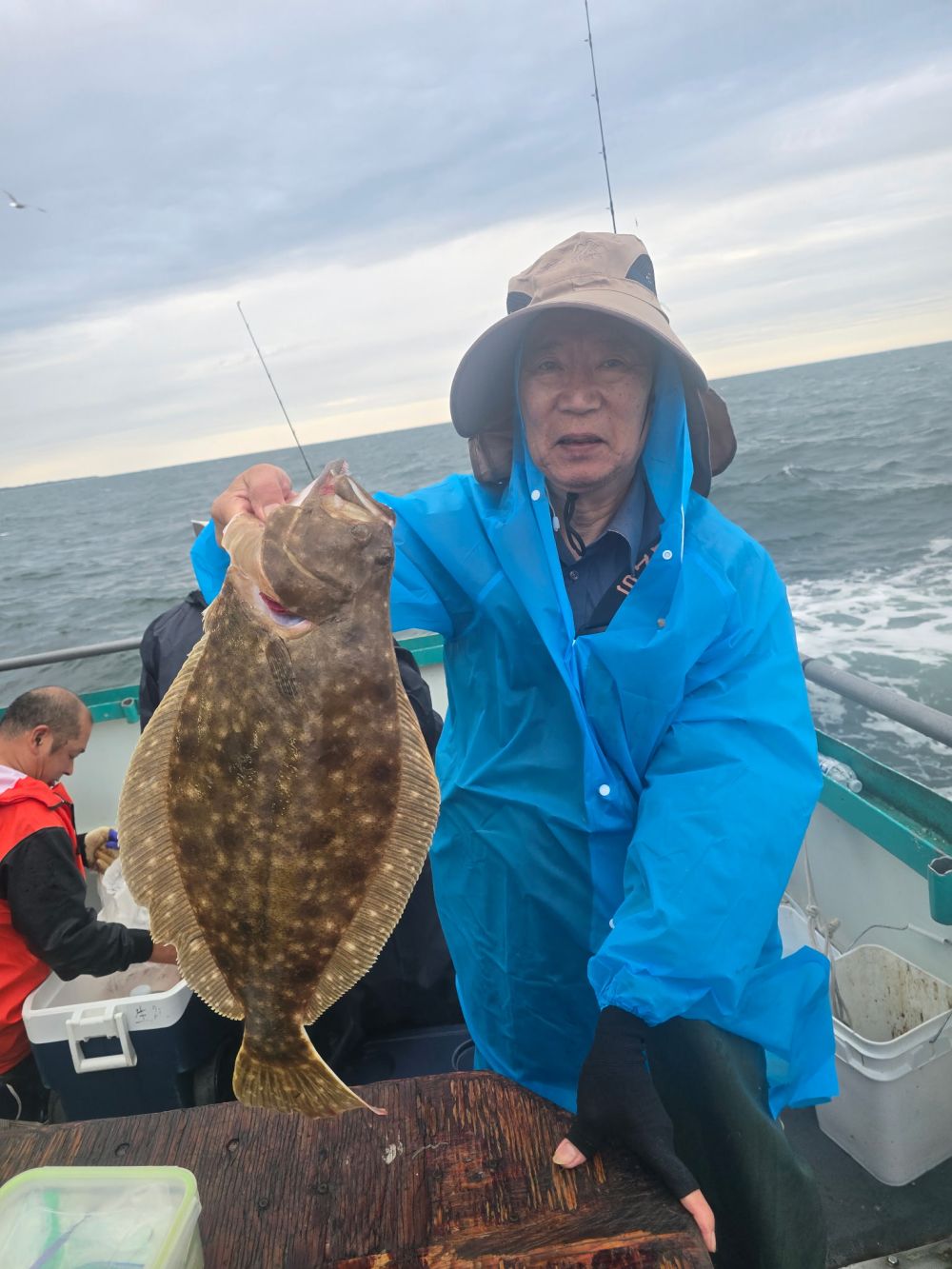Person in blue raincoat holding a large fish on a boat at sea.