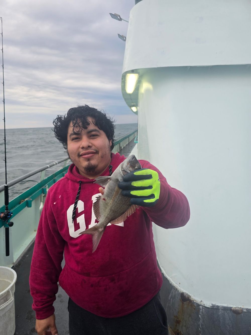 Person in red hoodie holding a fish on a boat at sea.