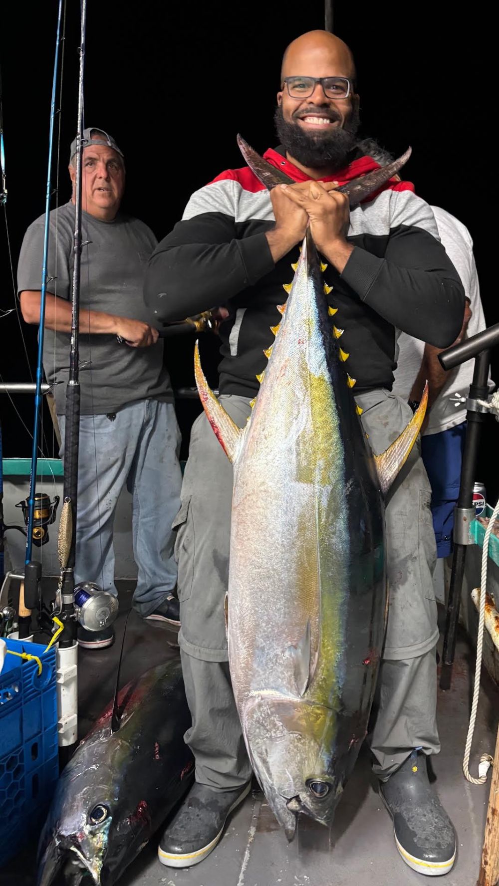 Man smiling and holding a large fish on a fishing boat at night.