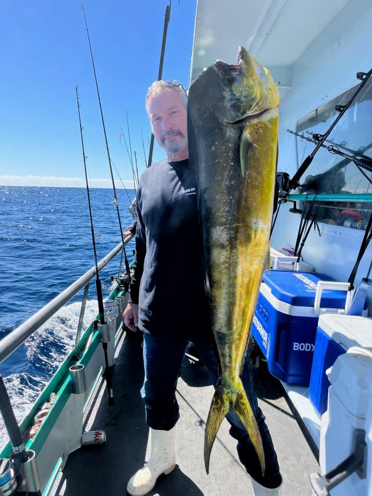 Person on boat holding a large fish, with ocean and fishing rods in background.