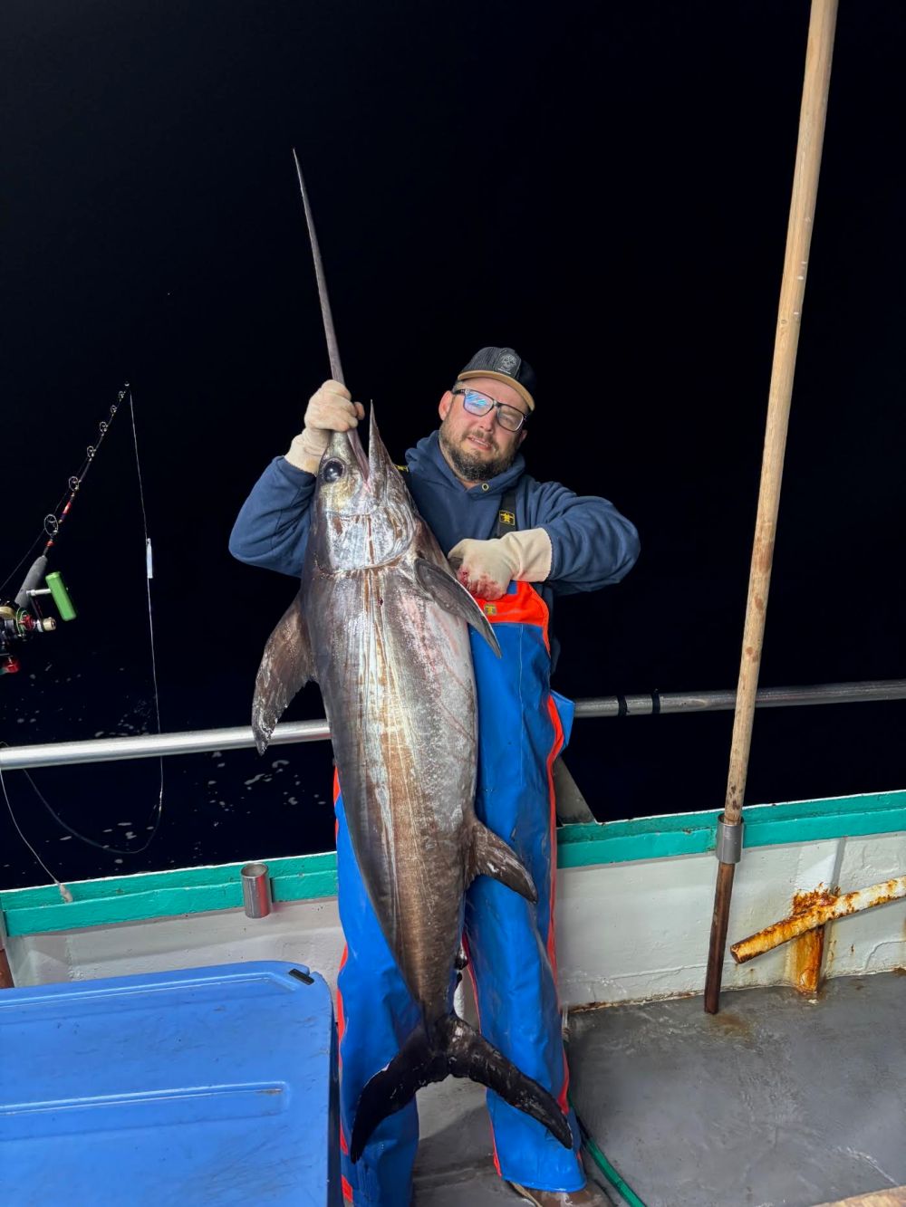 Person on a boat holding a large swordfish at night.