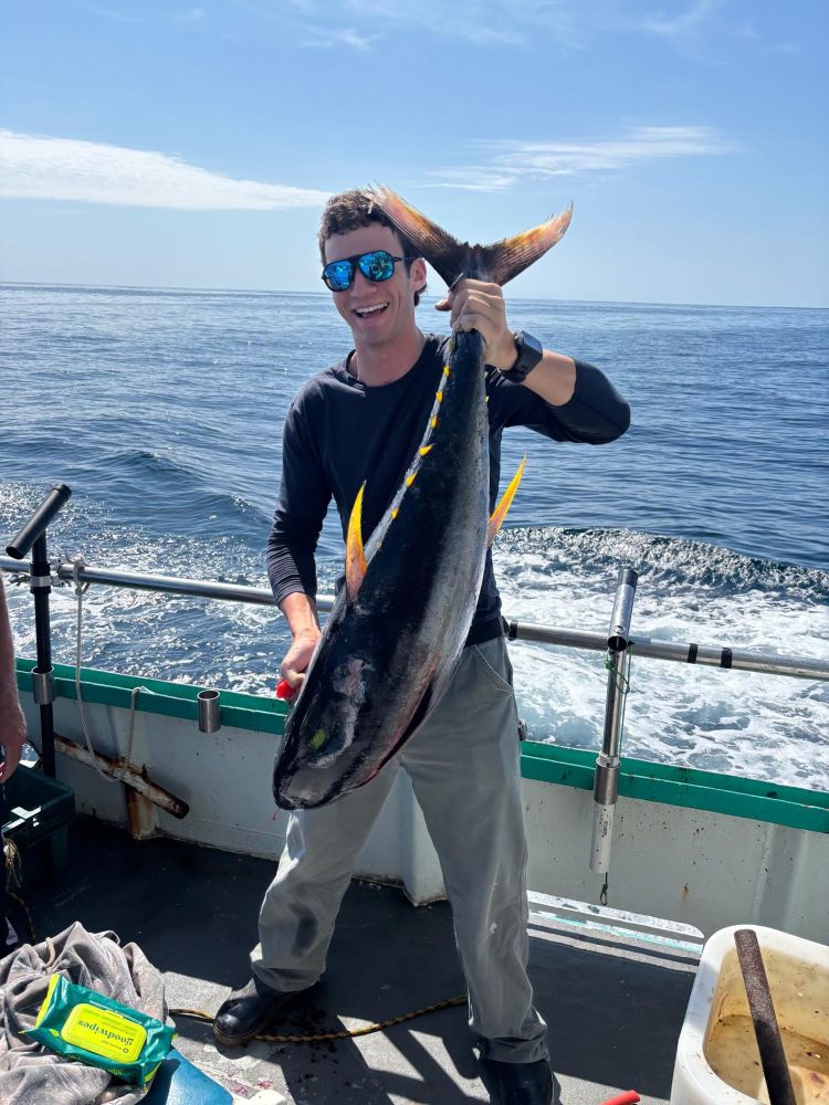 Man on boat holding large fish, ocean and sky in background.