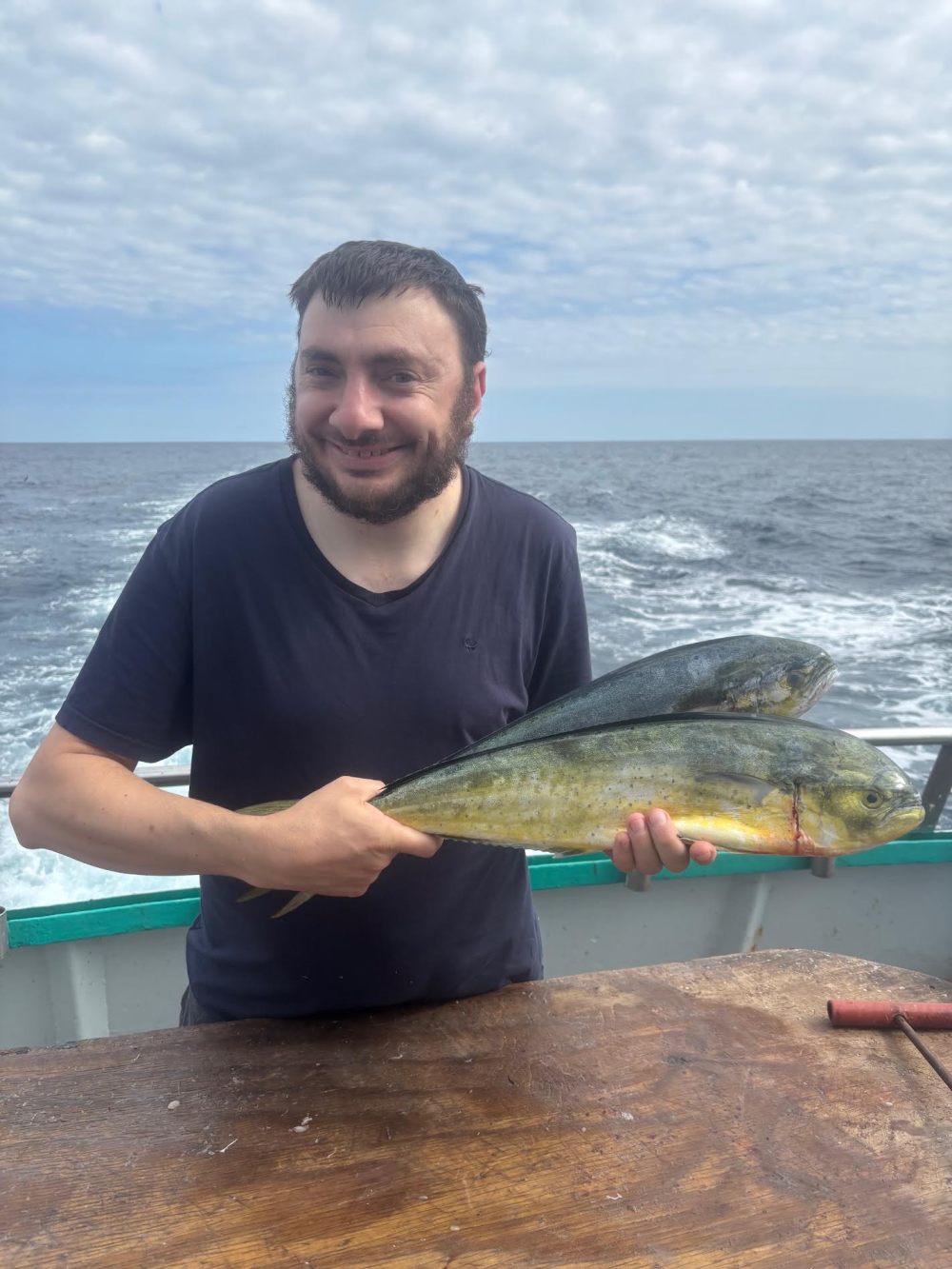 Man on boat holding a freshly caught fish under cloudy sky.