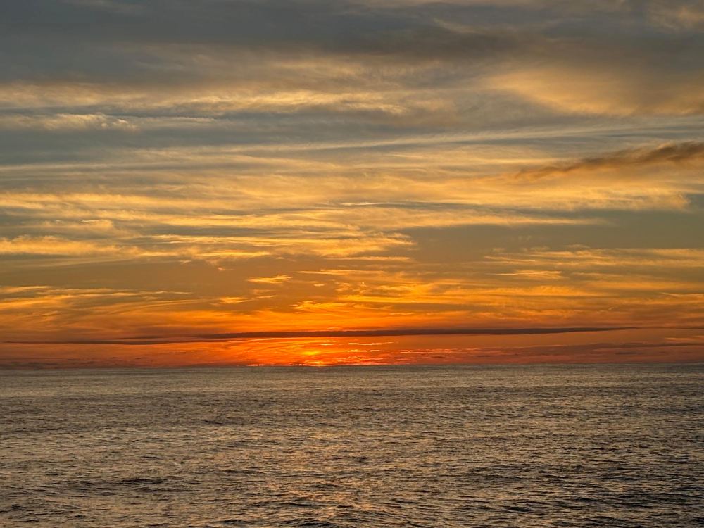 Ocean sunset with orange sky and scattered clouds.