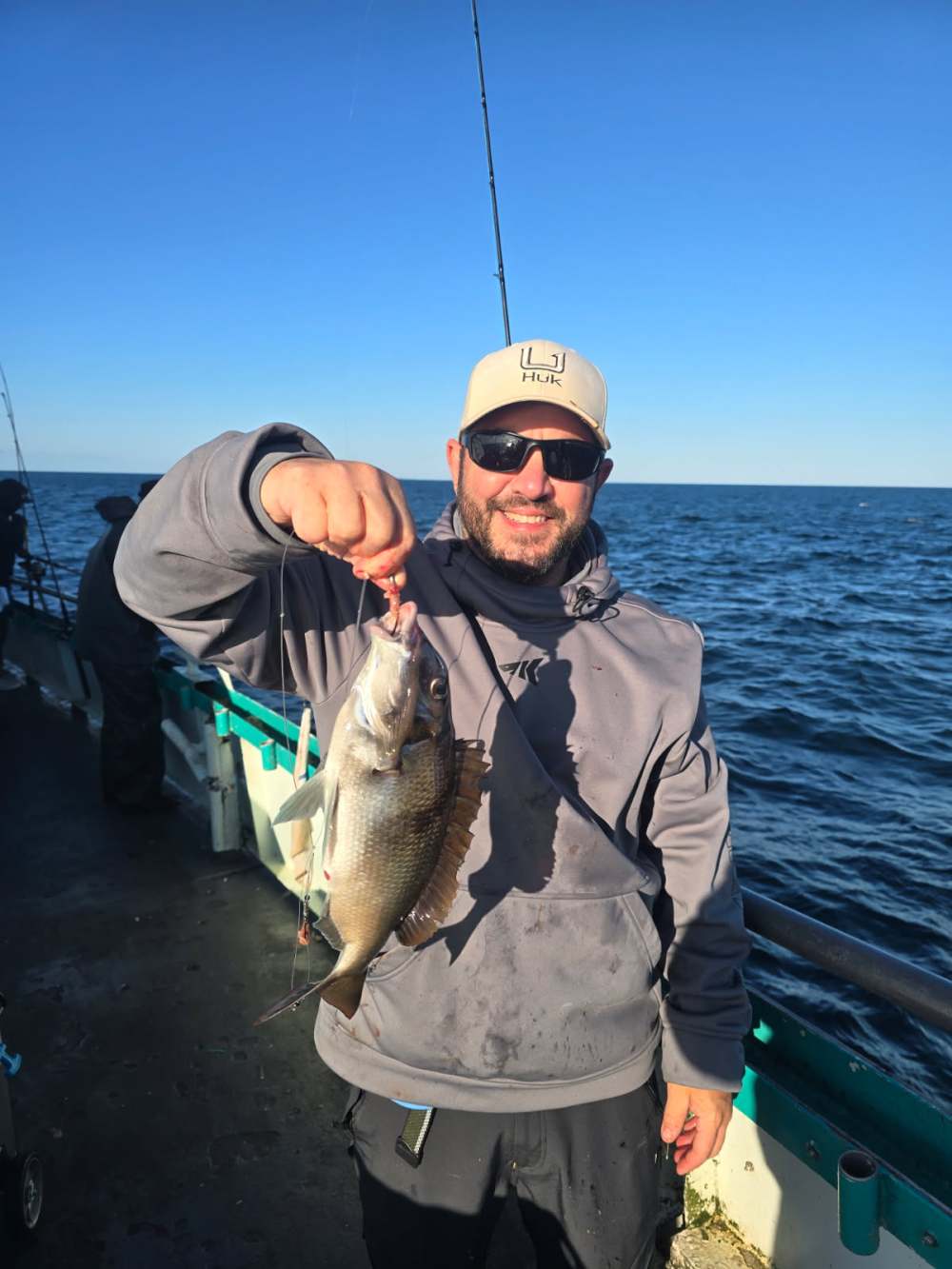 Man on a boat holding a fish with the ocean in the background.