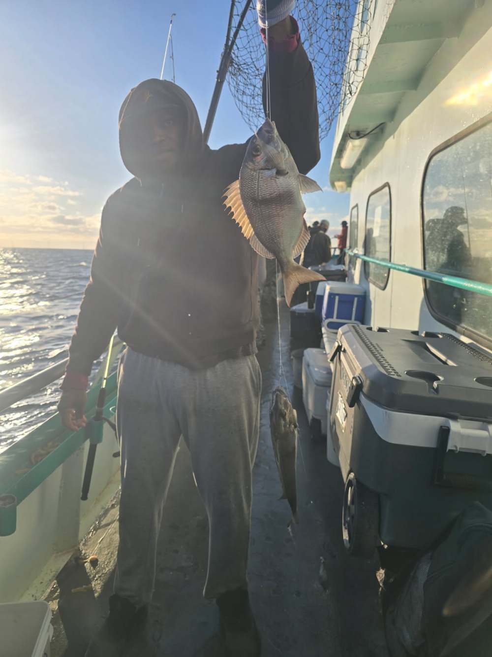 Person on boat holding a fish in sunlight.