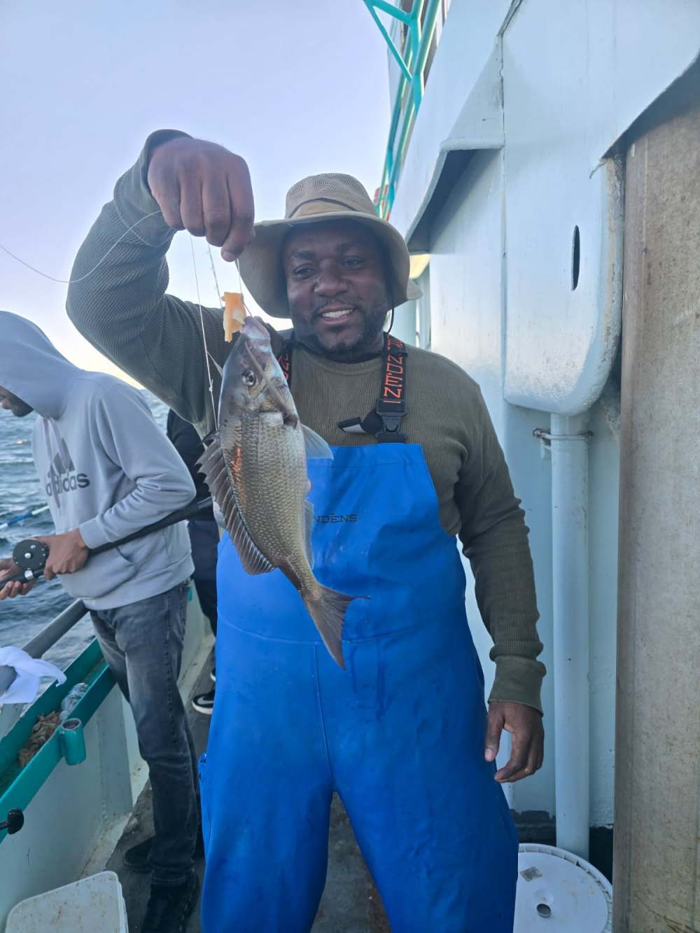 Man in blue overalls holding a fish on a boat.