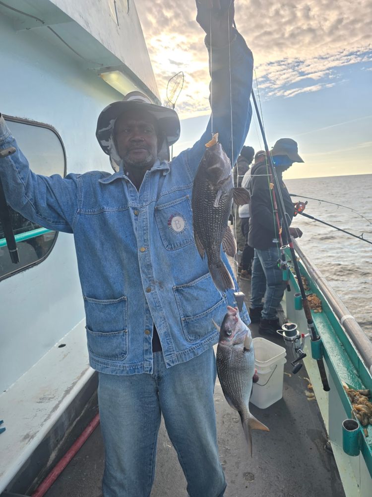 Man on boat holding two fish, others fishing in background.