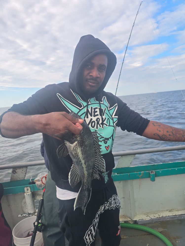 Person on a boat holding a fish, wearing a hoodie and sweatpants.