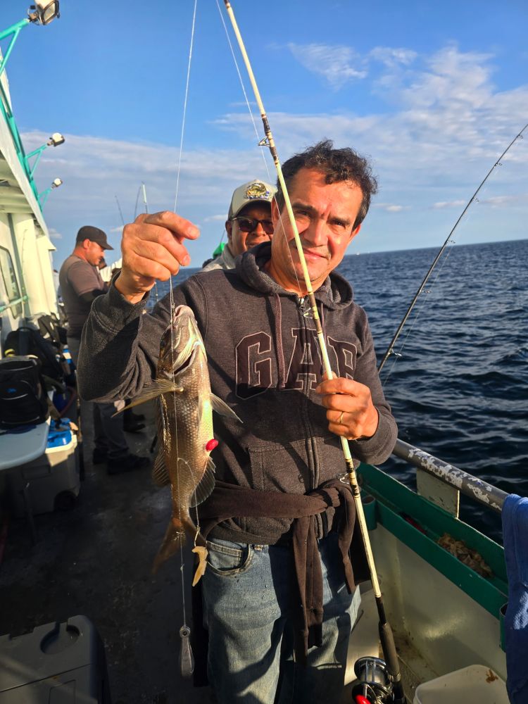 Man holding a fish on a fishing boat with others in the background.