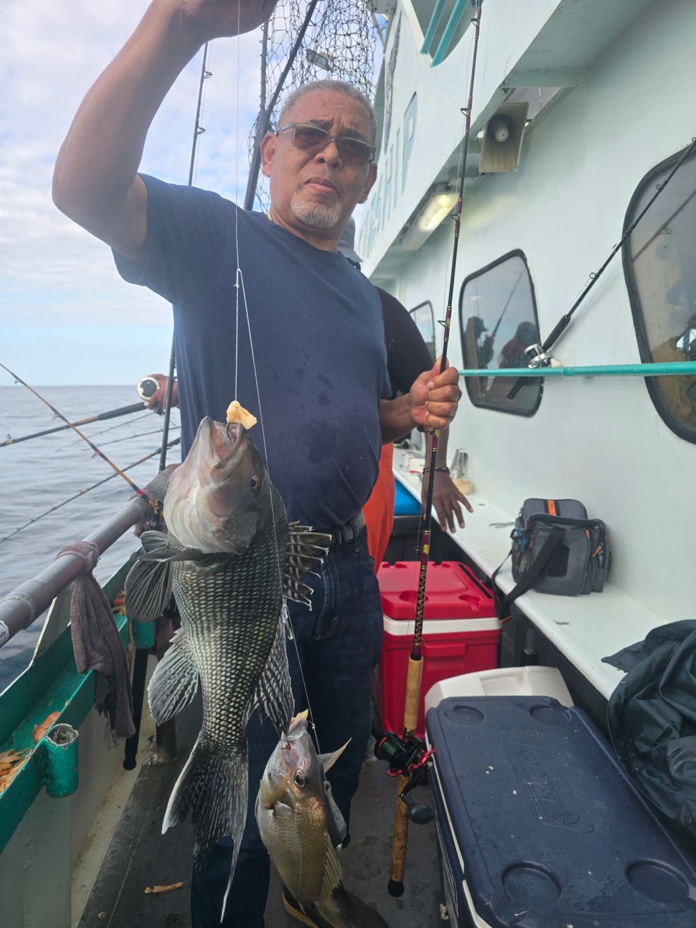 Man on a boat holding a fishing rod and three caught fish.