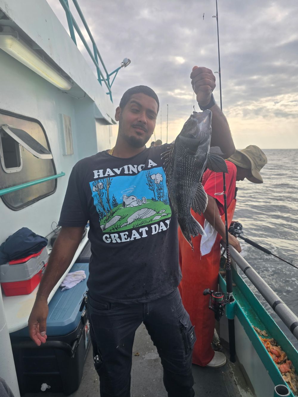 Man on a boat holding a large fish, wearing a 'Having a Great Day' shirt.