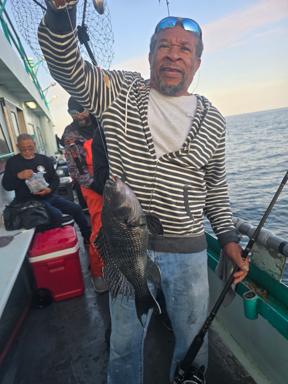 Man holding a fish on a boat, others in the background.