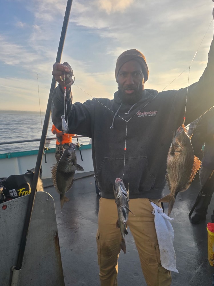 Person on boat holding multiple fish on a line at sunset.