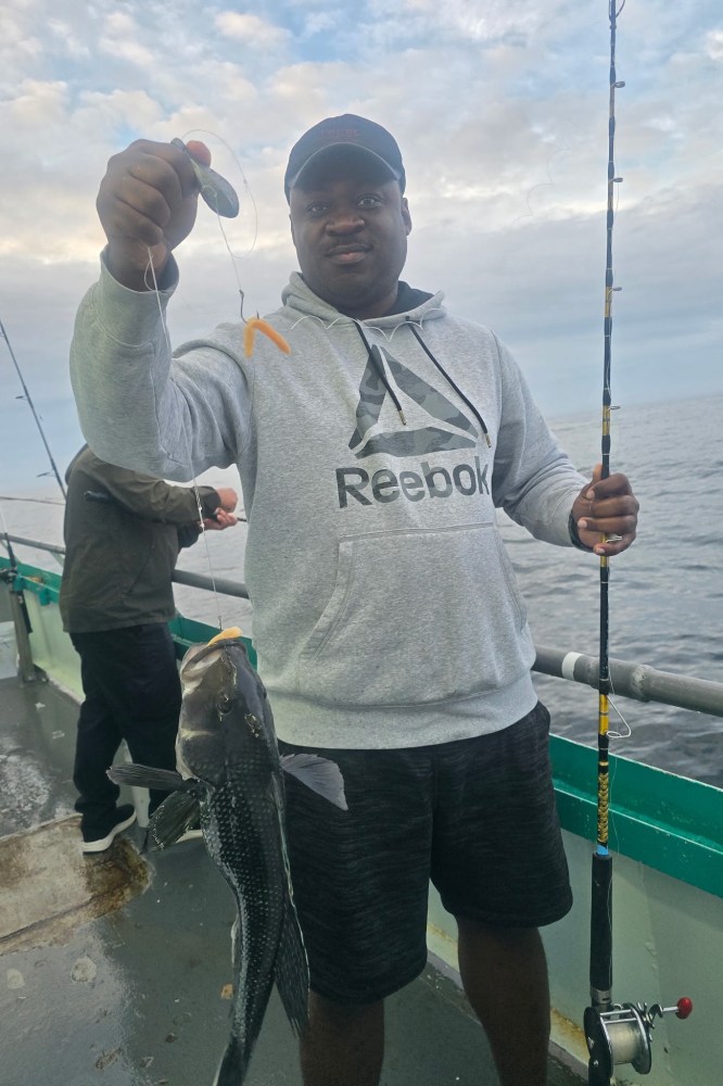 Man holding fishing rod and fish on boat deck with ocean view.