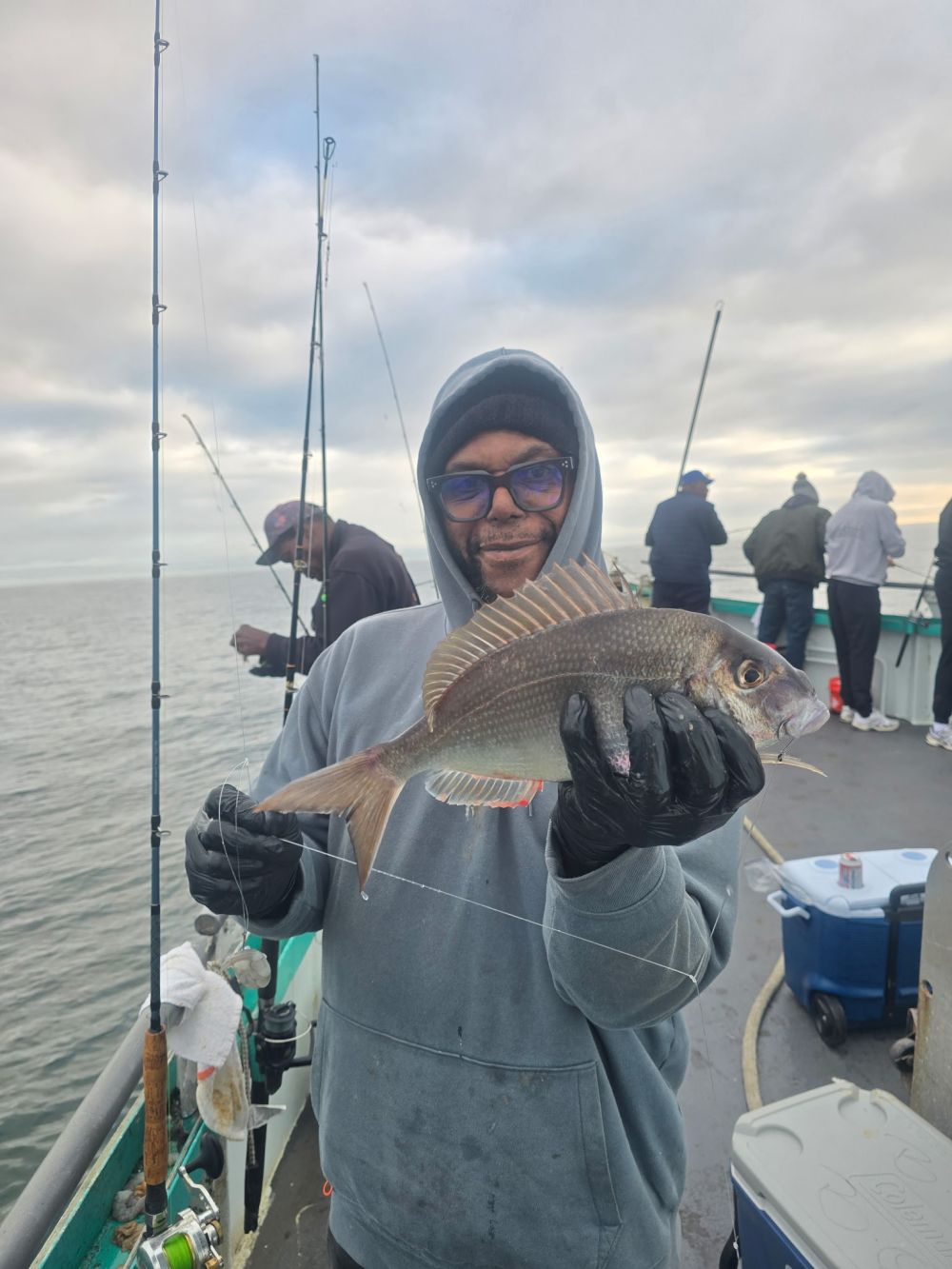 Person holding a fish on a boat, with fishing rods in the background.