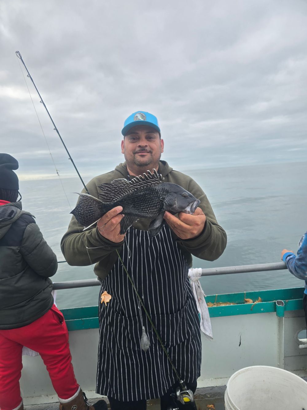 Man holding fish on a boat, wearing a striped apron and blue cap.