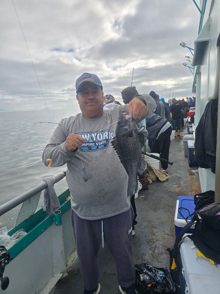 Man holding a fish on a boat, with cloudy sky and other people in the background.
