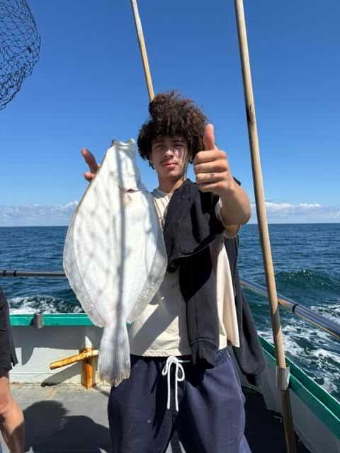Person on boat holding a flatfish under a clear sky.