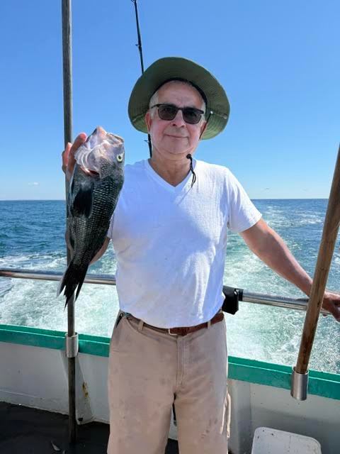 Man in a hat holding a fish on a boat with ocean in background.