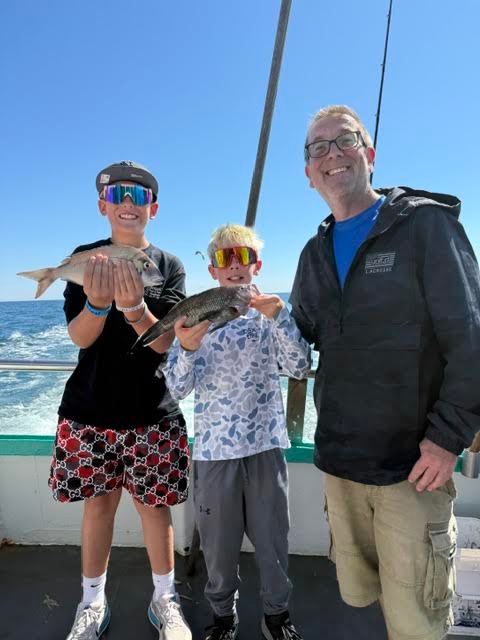 Three people on a boat holding fish, smiling at the camera.