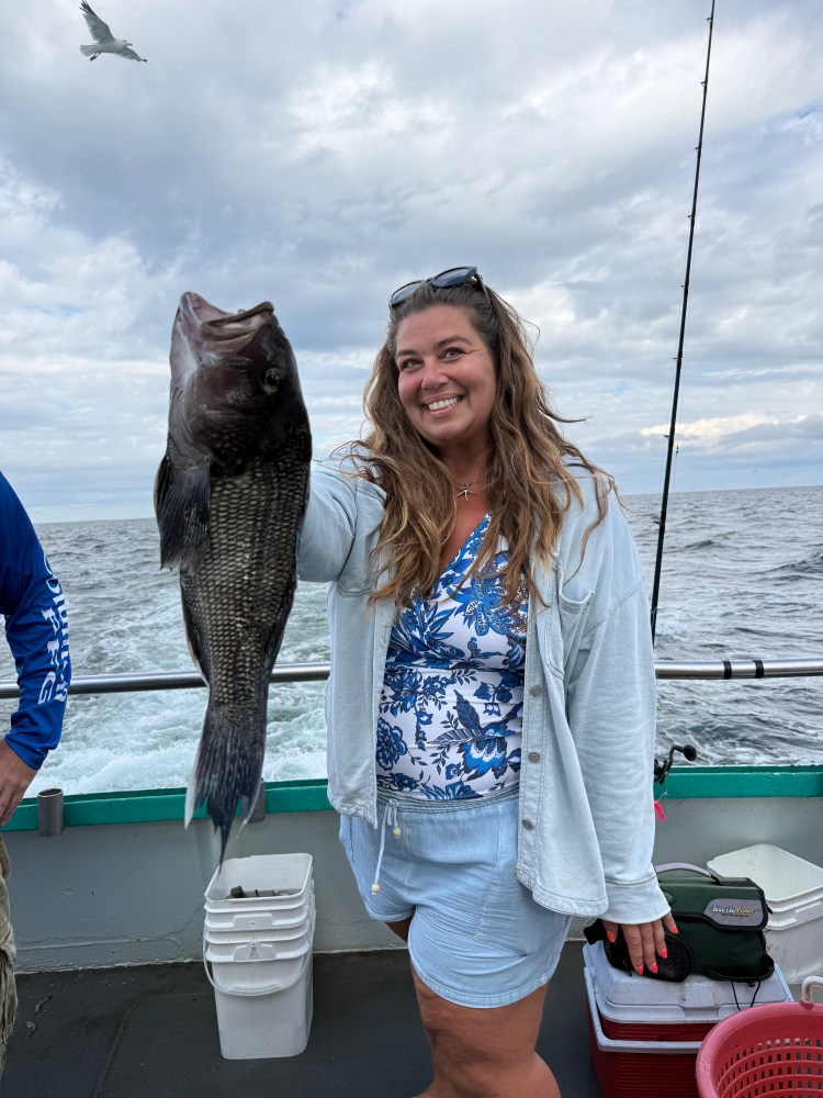 Woman smiling with large fish on a boat, cloudy sky and seagull above.