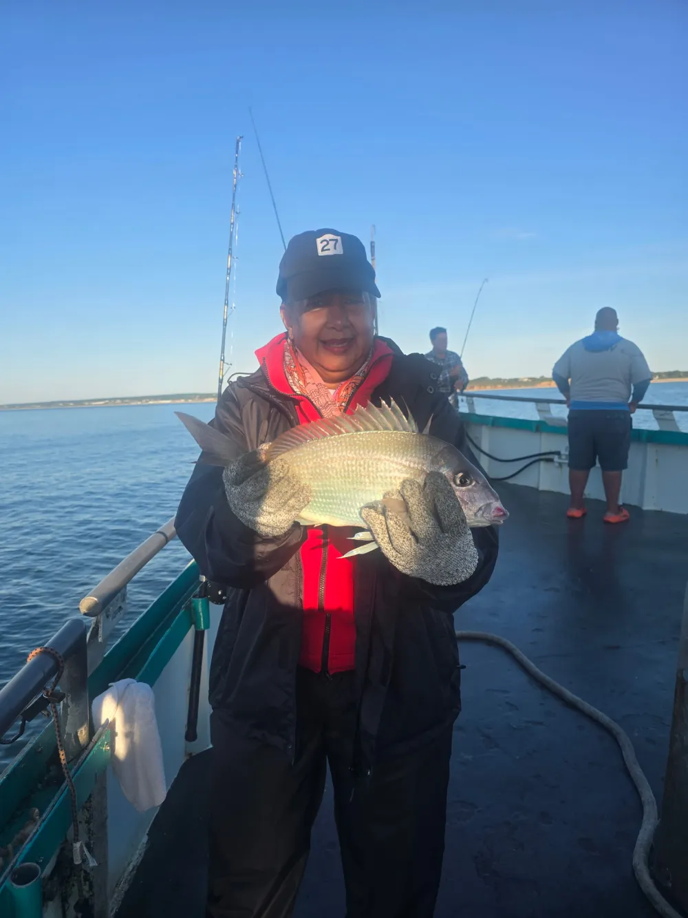 Person holding a fish on a boat with rods in the background.