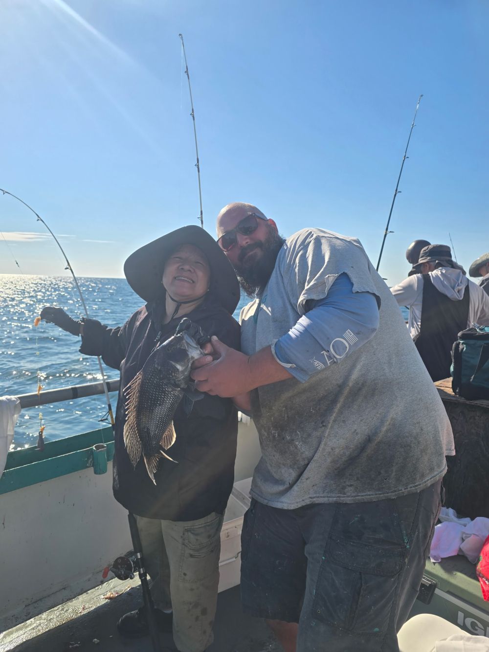Two people on a boat holding a fish with fishing rods in the background.