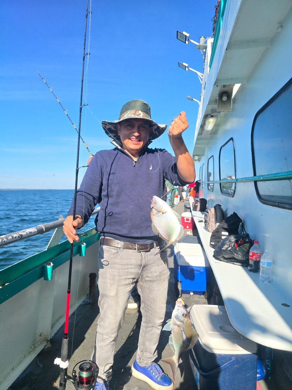 Man fishing on a boat with a hat, holding a small fish.