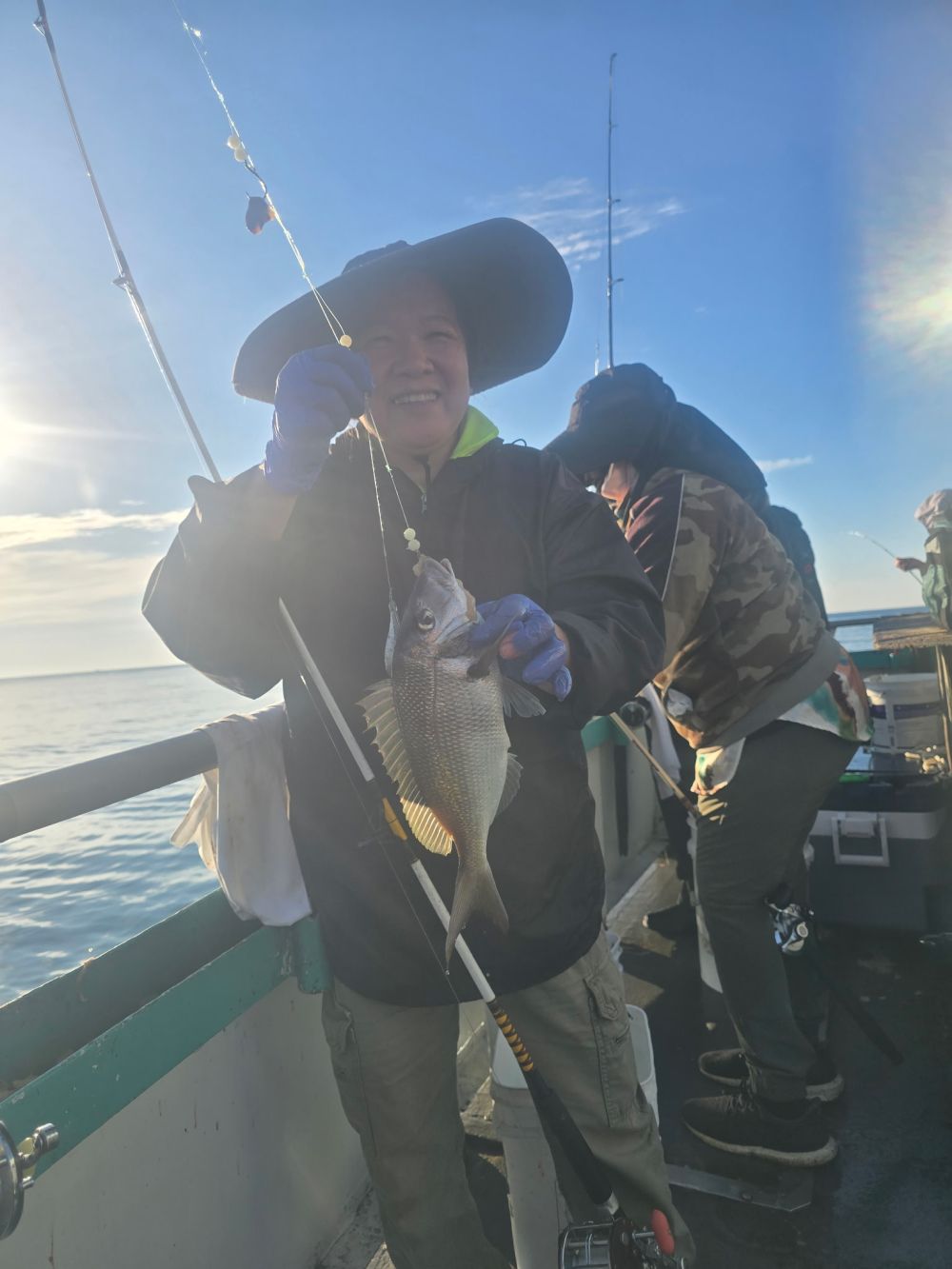 Person in a hat holding a fish on a boat with another person nearby.