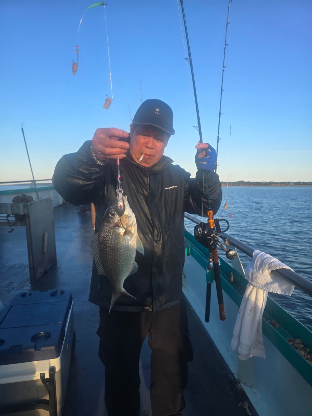 Person holding two fish on a boat, with fishing rods and an ocean backdrop.