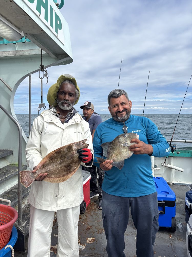 Two men on a boat holding caught fish, smiling at the camera.