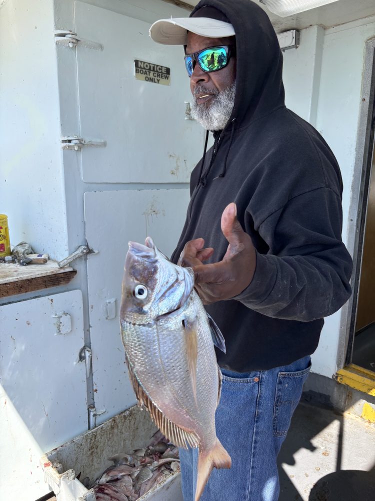 Person in sunglasses holding a fish on a boat.
