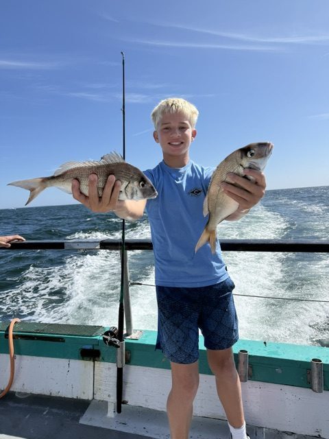 Person holding two fish on a boat with ocean in the background.