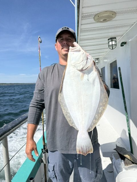 Person holding large fish on a boat with ocean in the background.