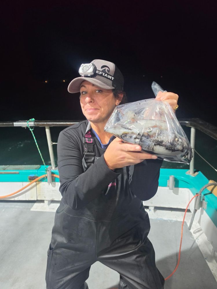 Person in cap holding a bag of fish on a boat at night.