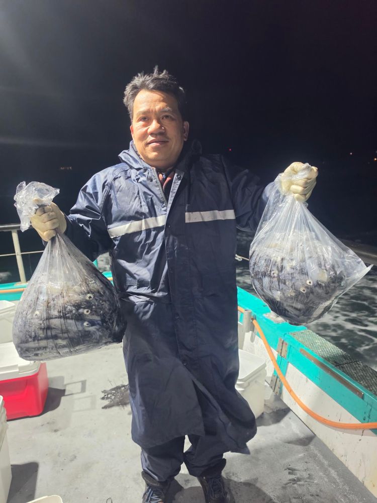 Person in a dark coat holding bags of fish on a boat at night.