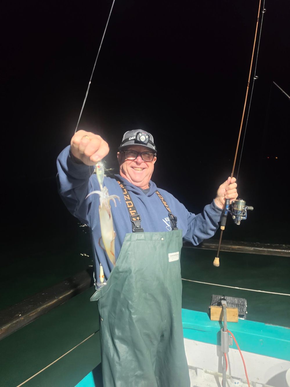 Person holding a fishing rod with a caught squid on a boat at night.