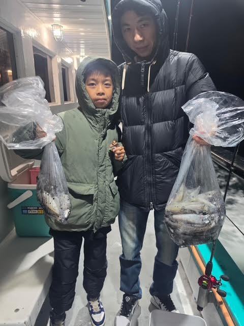 Two people on a boat holding bags of fish at night.