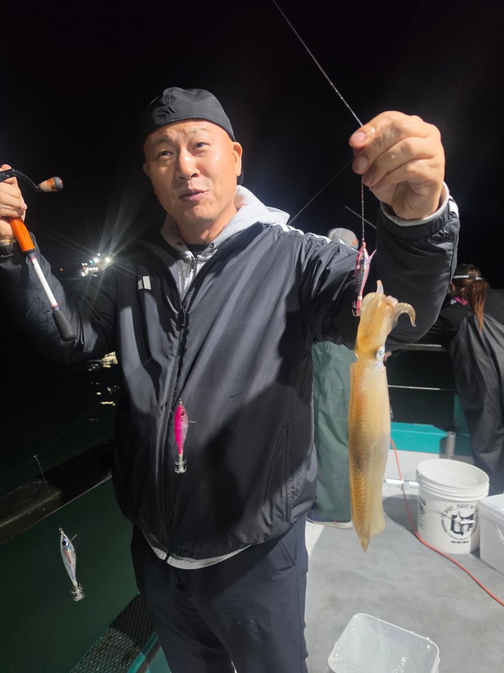 Person holding a caught squid on a boat at night.