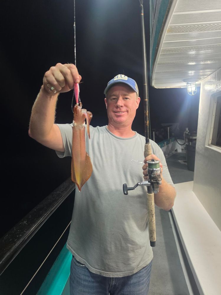Man holding fishing rod with squid on boat at night.