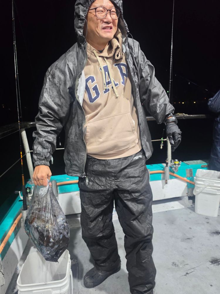 Person in rain gear holding a bag on a boat at night.